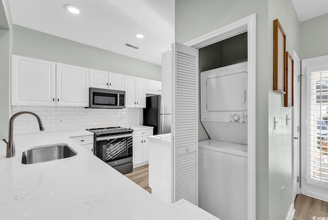 kitchen featuring stacked washer and dryer, tasteful backsplash, white cabinets, appliances with stainless steel finishes, and a sink