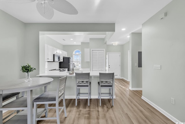 kitchen with light wood finished floors, appliances with stainless steel finishes, light countertops, a kitchen bar, and white cabinetry