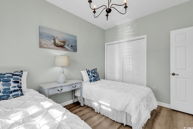 bedroom with baseboards, a closet, wood finished floors, and a notable chandelier