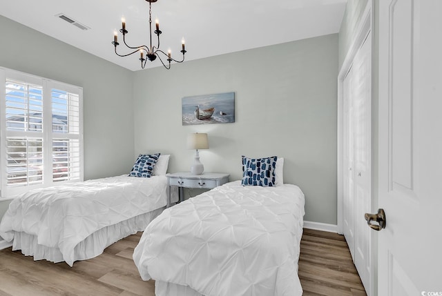 bedroom featuring an inviting chandelier, baseboards, visible vents, and wood finished floors