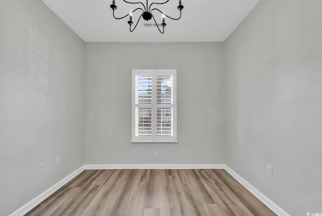 unfurnished room featuring a notable chandelier and light wood-type flooring