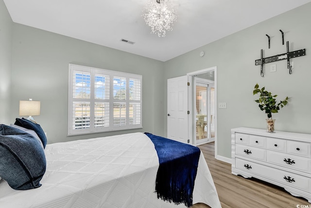 bedroom featuring light wood finished floors, baseboards, visible vents, and a notable chandelier