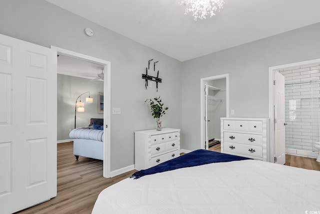 bedroom featuring a spacious closet, ensuite bath, wood finished floors, and baseboards