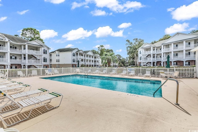 community pool with a patio, fence, and a residential view