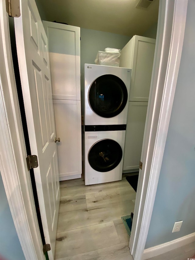 laundry room with cabinets, light wood-type flooring, and stacked washing maching and dryer