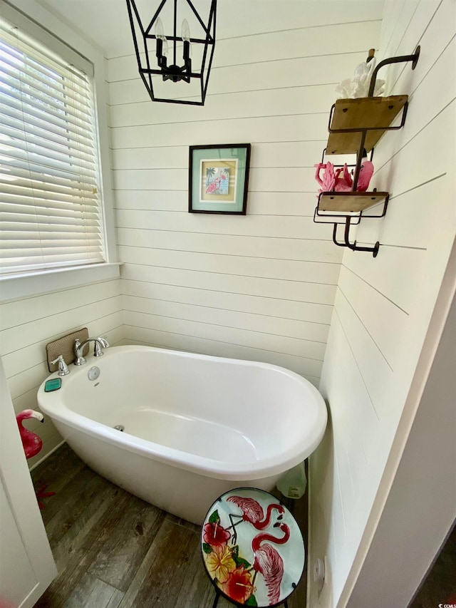 bathroom with a tub to relax in, wooden walls, and hardwood / wood-style floors