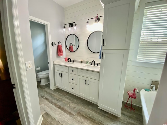 bathroom featuring hardwood / wood-style flooring, a bathtub, wood walls, vanity, and toilet