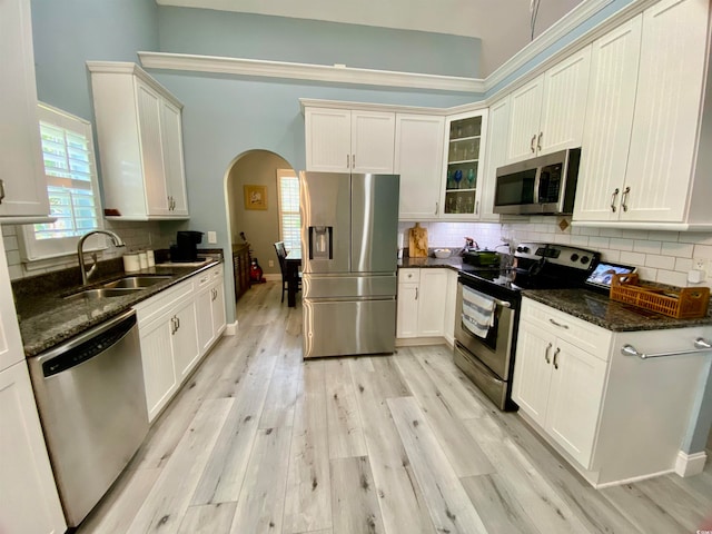 kitchen with sink, light hardwood / wood-style flooring, appliances with stainless steel finishes, dark stone counters, and decorative backsplash