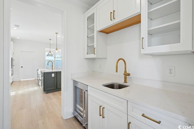 kitchen featuring beverage cooler, hanging light fixtures, light stone counters, sink, and white cabinetry