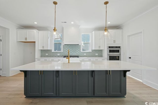 kitchen with stainless steel double oven, custom exhaust hood, gray cabinetry, and a large island with sink