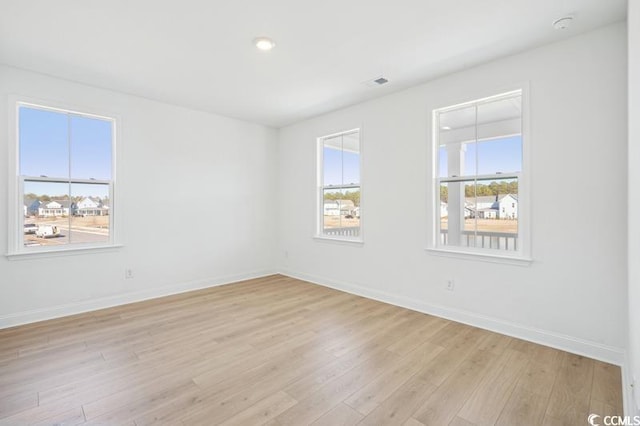 empty room featuring visible vents, a healthy amount of sunlight, light wood-style flooring, and baseboards