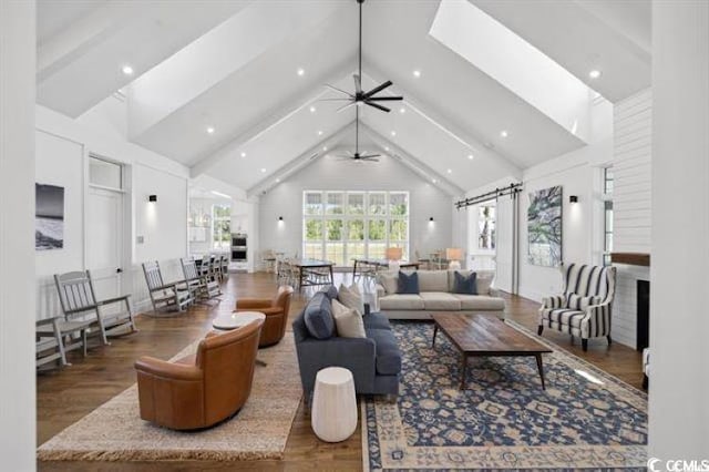 living area with beam ceiling, high vaulted ceiling, ceiling fan, and wood finished floors