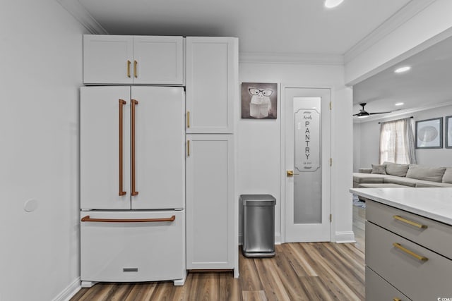 kitchen featuring wood-type flooring, crown molding, white cabinets, light stone counters, and built in fridge