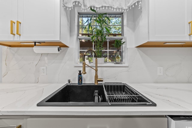 kitchen with tasteful backsplash, white cabinets, light stone countertops, and sink