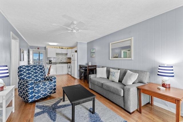 living room featuring ceiling fan, light wood-type flooring, and crown molding