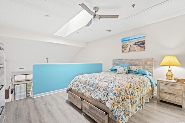 bedroom featuring ceiling fan, vaulted ceiling with skylight, light hardwood / wood-style flooring, and a textured ceiling