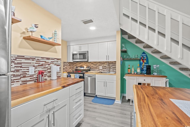 kitchen with white cabinets, backsplash, stainless steel appliances, wooden counters, and light wood-type flooring