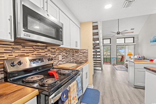 kitchen featuring decorative backsplash, white cabinets, butcher block counters, stainless steel appliances, and light hardwood / wood-style flooring