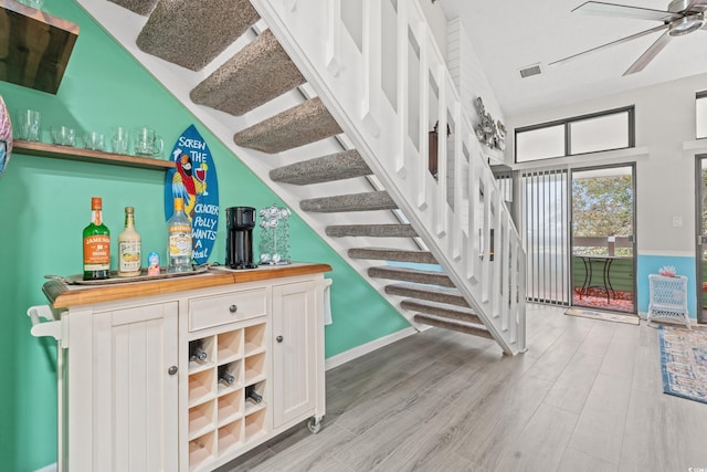 stairway featuring wood finished floors, visible vents, a ceiling fan, and a bar