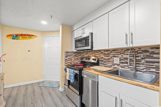 kitchen with white cabinets, stainless steel appliances, a sink, light wood-style floors, and baseboards
