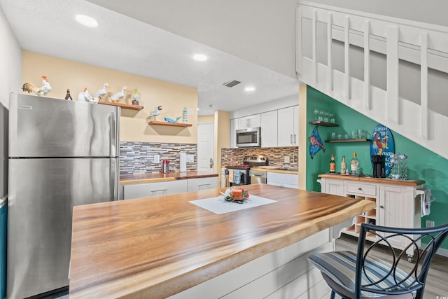 kitchen with stainless steel appliances, open shelves, visible vents, decorative backsplash, and wood counters