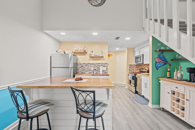 kitchen featuring tasteful backsplash, light wood-style floors, butcher block countertops, appliances with stainless steel finishes, and a breakfast bar area
