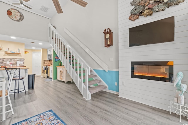 interior space featuring wood-type flooring, a high ceiling, a large fireplace, and ceiling fan