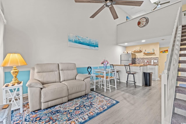 living room with a towering ceiling, wood finished floors, baseboards, stairs, and ceiling fan