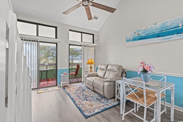 living area featuring a wainscoted wall, wood finished floors, visible vents, a ceiling fan, and high vaulted ceiling
