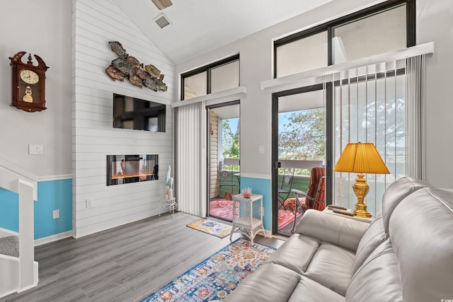 living area featuring visible vents, baseboards, wood finished floors, a large fireplace, and high vaulted ceiling