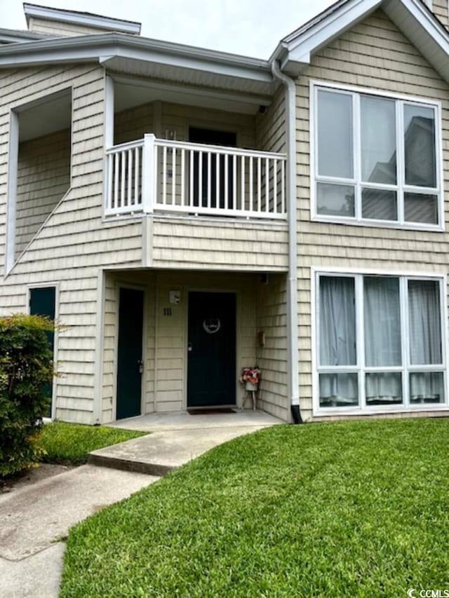 view of front of house featuring a balcony, a patio, and a front lawn