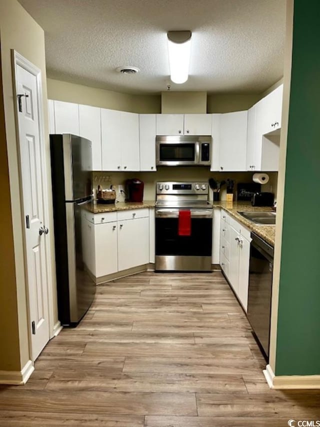 kitchen featuring a textured ceiling, light hardwood / wood-style floors, sink, white cabinetry, and appliances with stainless steel finishes