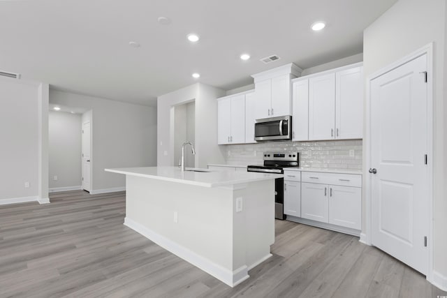 623 Blackthorne Cir NW, Calabash, NC 28467 - kitchen with appliances with stainless steel finishes, a kitchen island with sink, light wood-type flooring, decorative backsplash, and white cabinetry