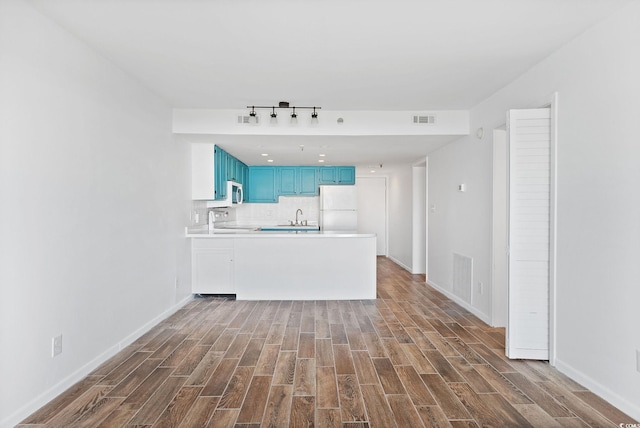 kitchen with wood-type flooring, white refrigerator, sink, kitchen peninsula, and blue cabinets