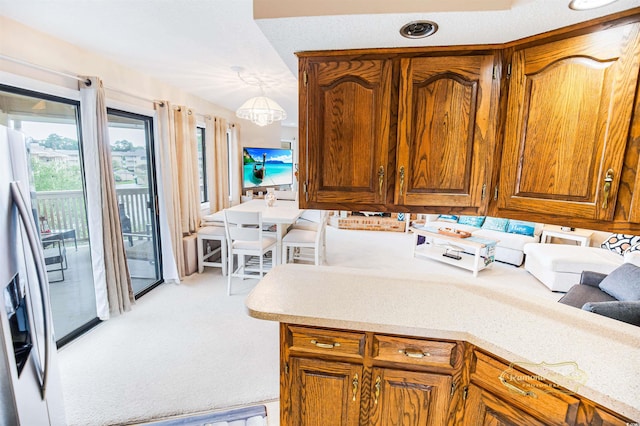 kitchen with light colored carpet, hanging light fixtures, and stainless steel fridge