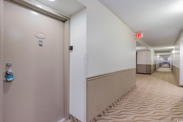 hallway featuring light colored carpet and a textured ceiling