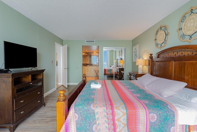 bedroom featuring a textured ceiling, light hardwood / wood-style flooring, and connected bathroom