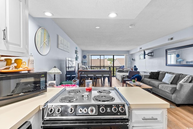 kitchen featuring white cabinets, stainless steel stove, a textured ceiling, and light wood-type flooring