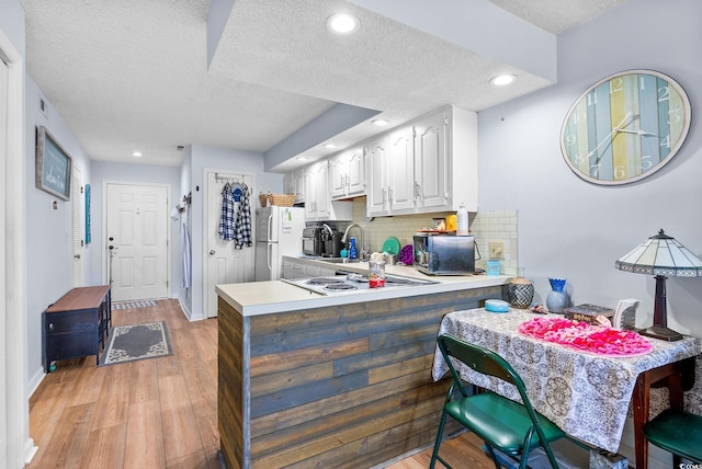 kitchen featuring light hardwood / wood-style floors, a textured ceiling, white cabinets, kitchen peninsula, and decorative backsplash