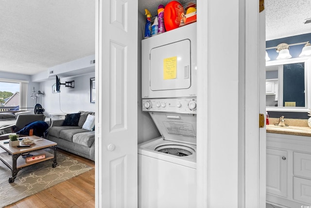 laundry area featuring a textured ceiling, stacked washer and clothes dryer, sink, and light hardwood / wood-style flooring