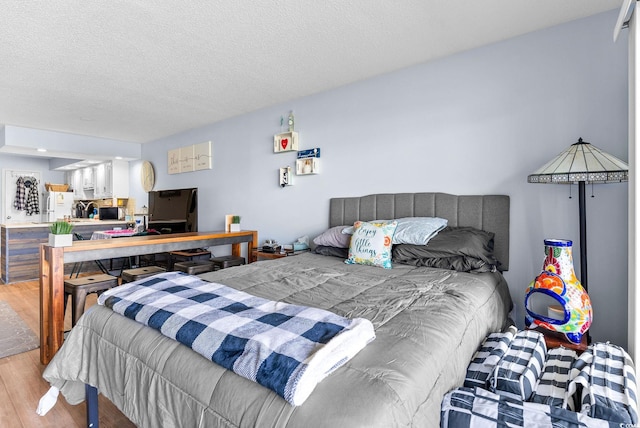 bedroom featuring fridge, light hardwood / wood-style floors, white fridge, and a textured ceiling