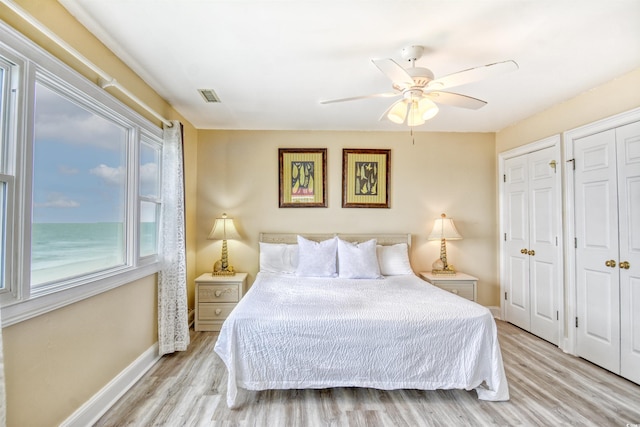 bedroom with light hardwood / wood-style flooring, multiple closets, and ceiling fan