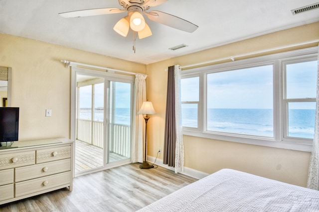 bedroom featuring ceiling fan, multiple windows, light hardwood / wood-style floors, and a water view