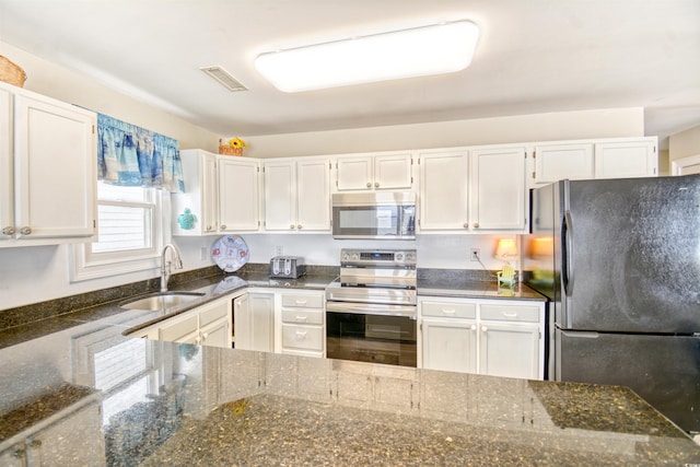 kitchen with dark stone countertops, appliances with stainless steel finishes, sink, and white cabinetry