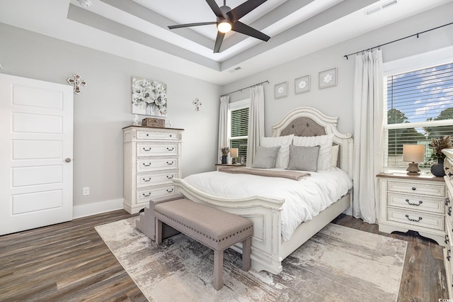 bedroom with multiple windows, a tray ceiling, dark wood-type flooring, and ceiling fan