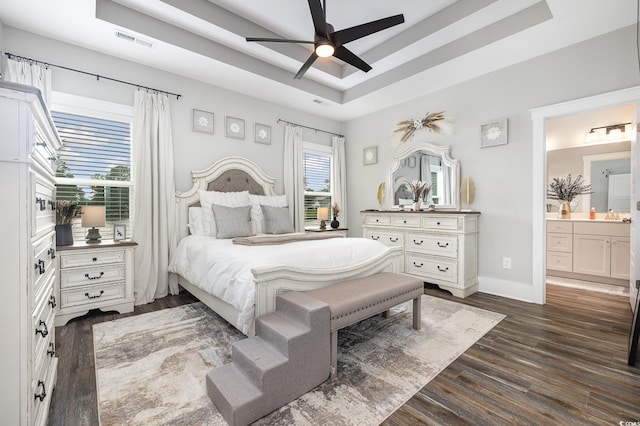 bedroom featuring ceiling fan, a tray ceiling, dark hardwood / wood-style floors, and ensuite bathroom