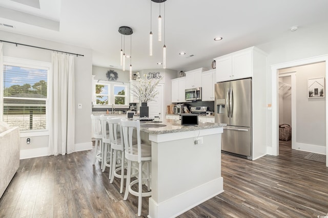 kitchen with pendant lighting, white cabinetry, stainless steel appliances, a center island, and dark hardwood / wood-style flooring