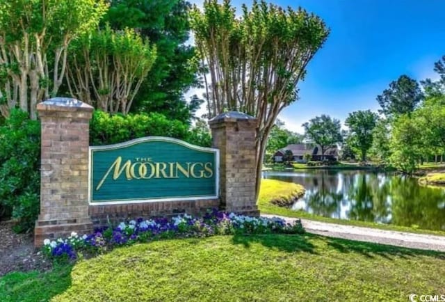 community / neighborhood sign featuring a lawn and a water view