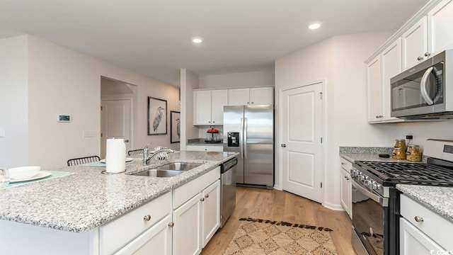 kitchen featuring light wood-type flooring, stainless steel appliances, white cabinetry, and a center island with sink