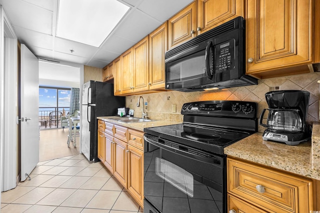 kitchen featuring a paneled ceiling, light stone countertops, light tile patterned flooring, black appliances, and sink